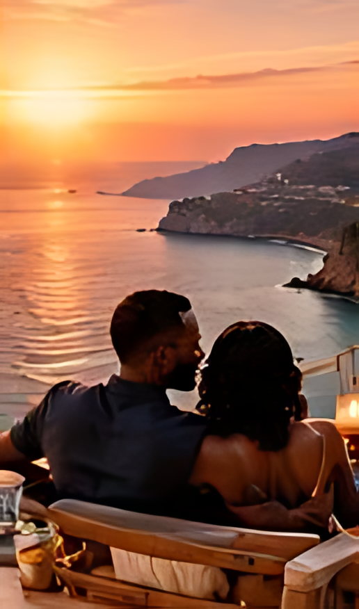 Two guests seated on a terrace with a bay below them at sunset